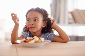 Girl at table eating fruit salad